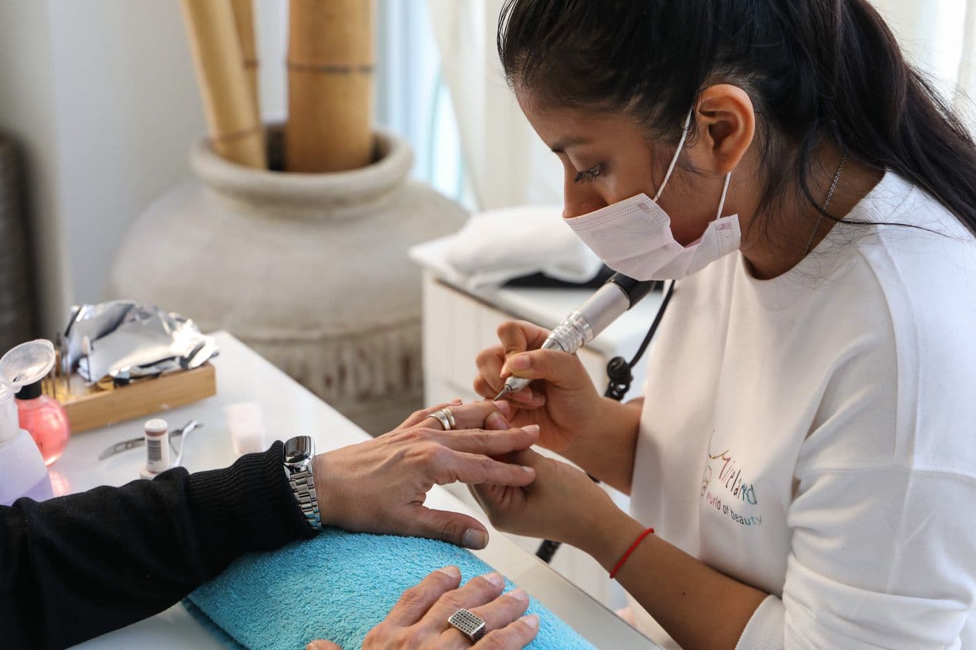 Una manicurista limando las uñas de su clienta sobre la mesa de trabajo.