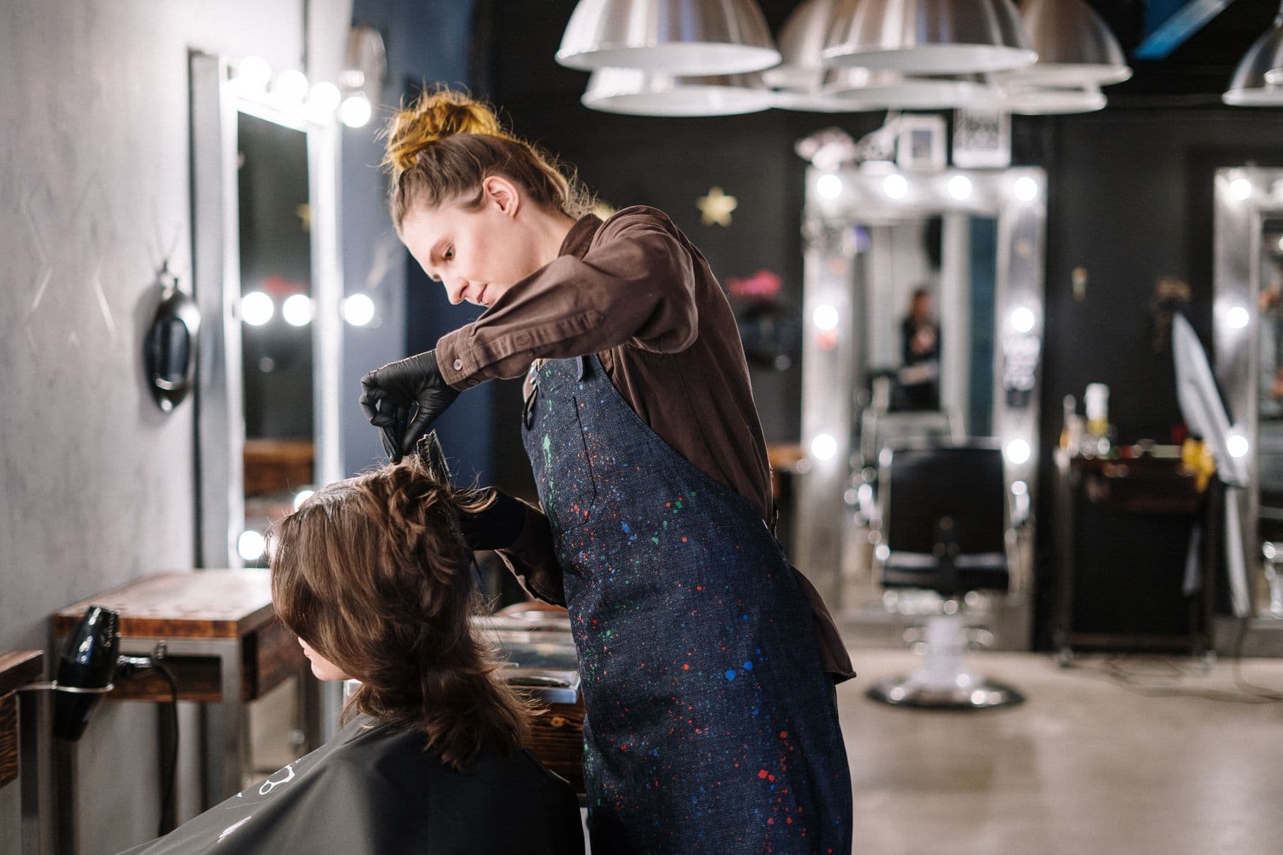 Una estilista trabajando el cabello de su clienta en un salón de belleza con espejos iluminados.