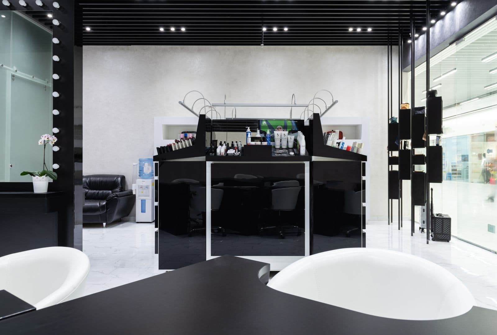 Un salón de belleza moderno, en blanco y negro, con sus puestos de trabajo y sus espejos iluminados.