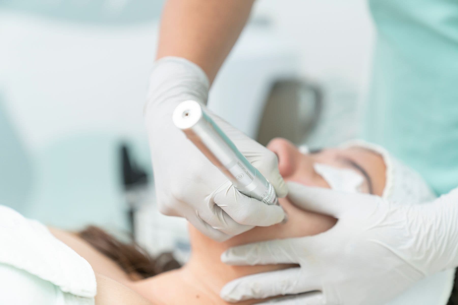 Una especialista con guantes aplicando un tratamiento facial con un equipo a una clienta recostada.