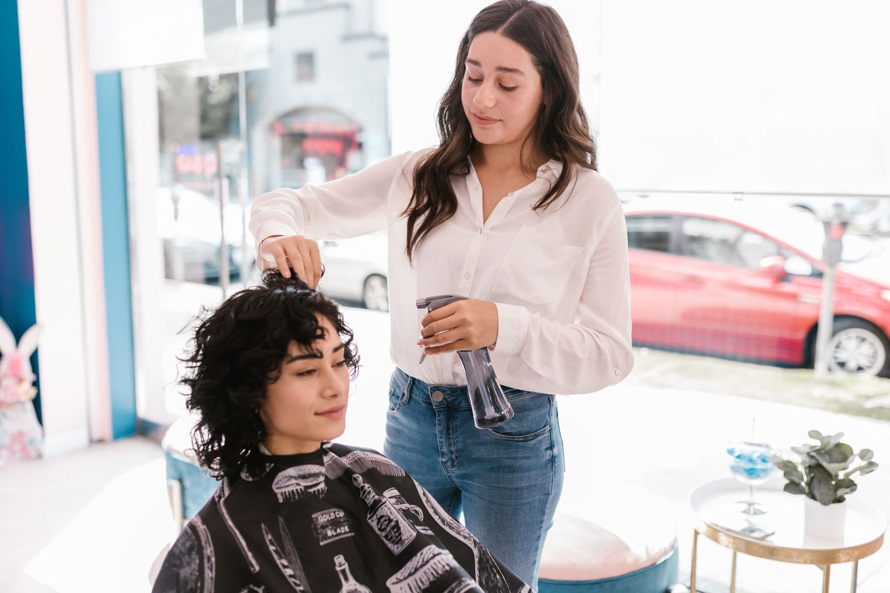Una estilista peinando a su clienta de pelo rizado en un salón luminoso.