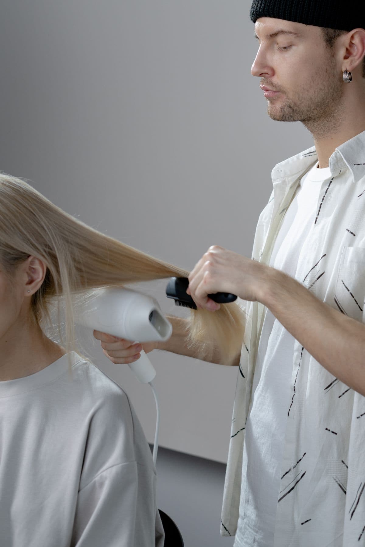 Un estilista secando con cepillo el pelo largo de una clienta.