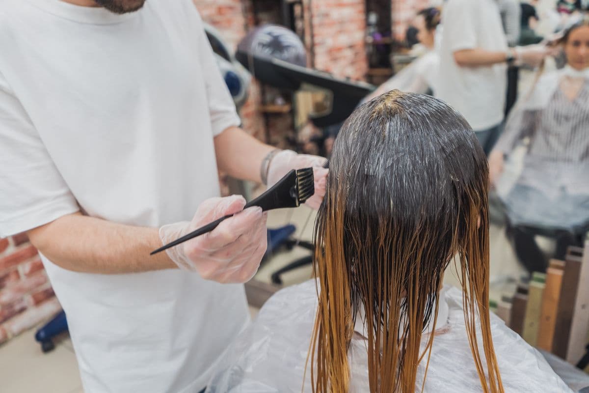 Una estilista aplicando tinte con brocha sobre el pelo largo de una clienta.