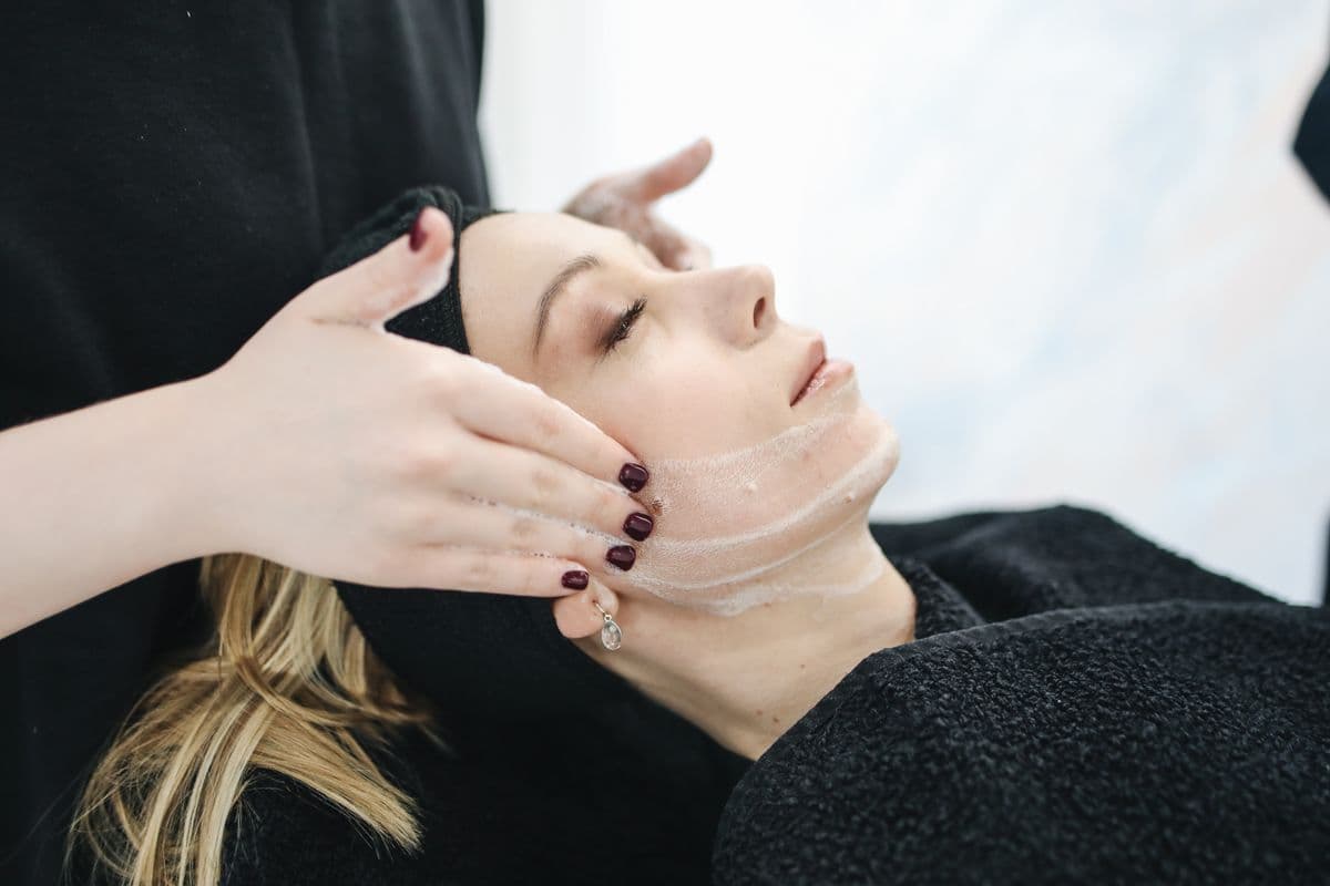 Una esteticista haciendo un masaje facial a una clienta con los ojos cerrados.
