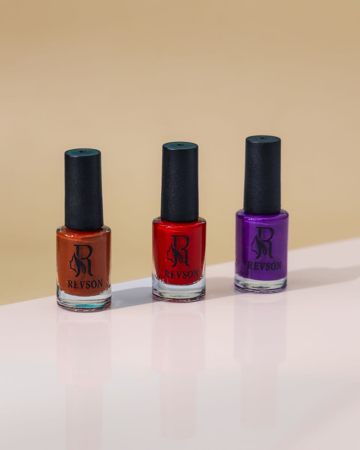 Tres frascos de esmalte en naranja, rojo y morado sobre una mesa.