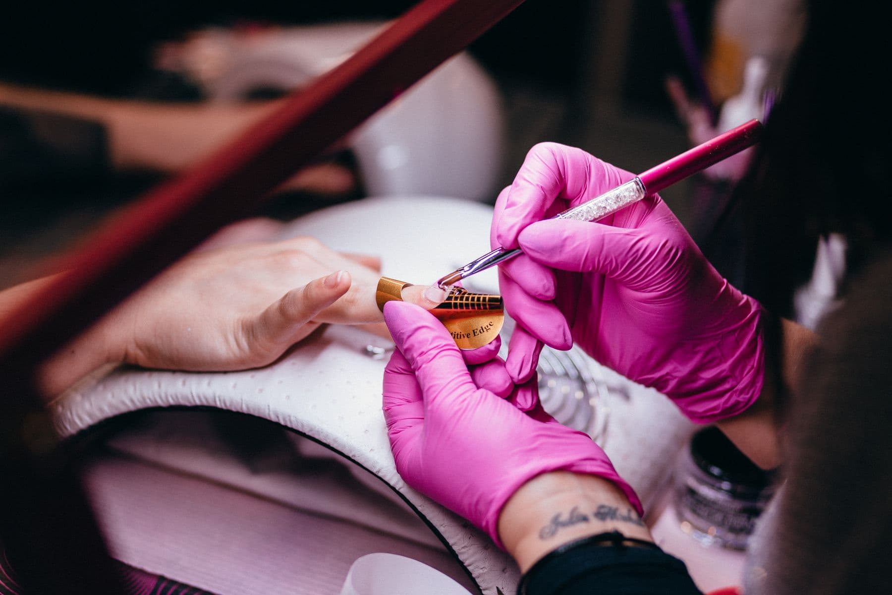 Una manicurista con guantes rosados pintando un diseño en las uñas de su clienta.