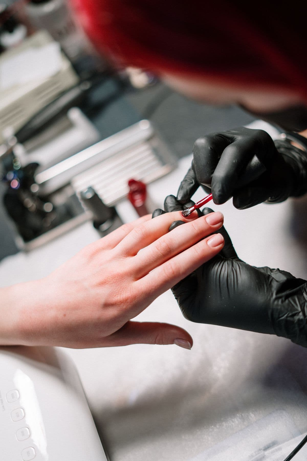 Una manicurista con guantes negros pintando las uñas de una clienta.